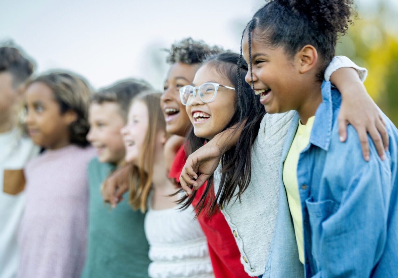 A diverse group of smiling kids with arms around each other enjoying a sunny outdoor moment. Celebrates friendship, unity, and playful teamwork among young friends.